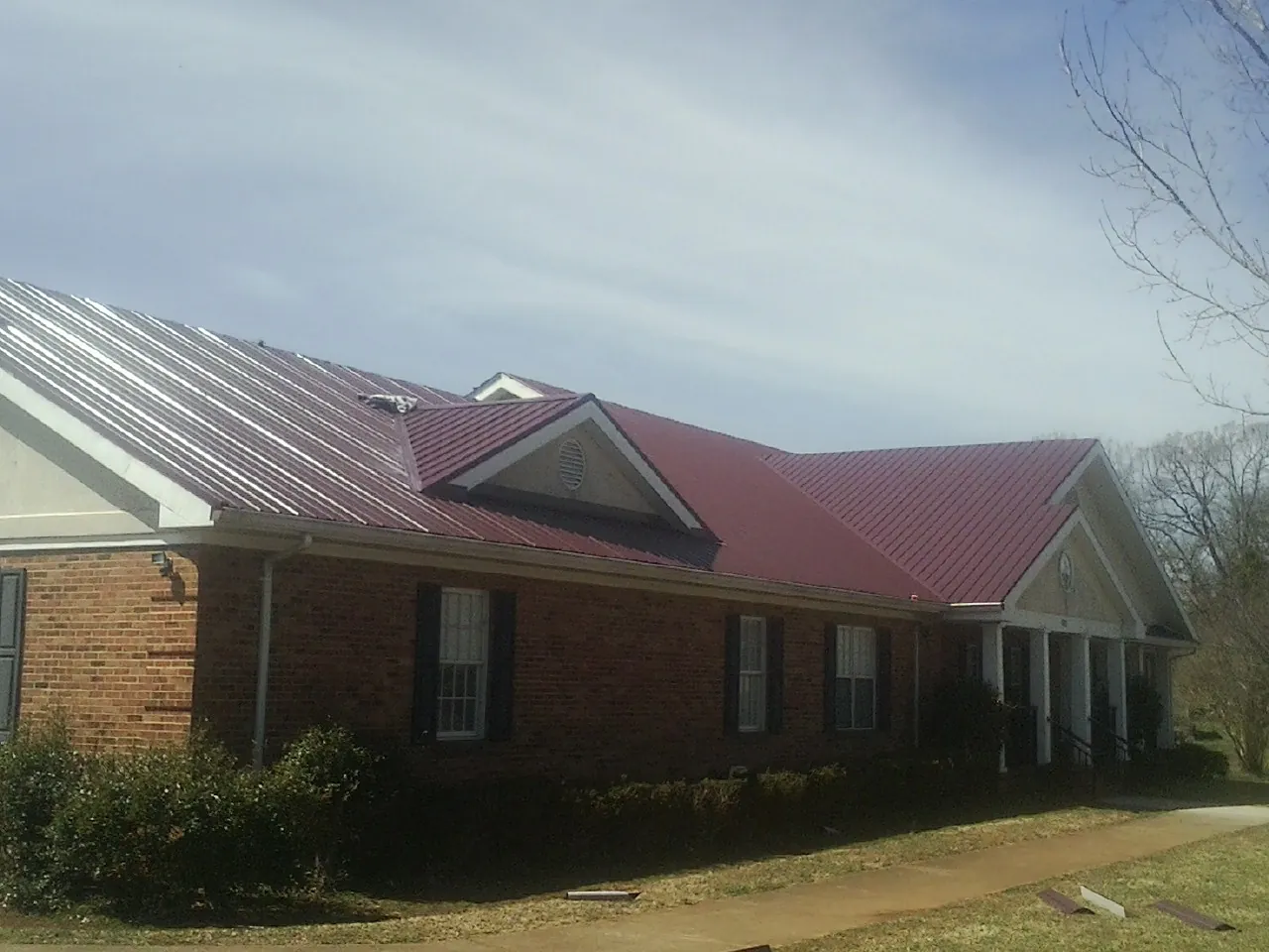 Red metal roof with gabled entries on a long brick building, from a Hail Damage Roof Repair job in Ward
