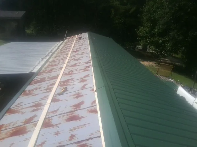 Old rusted panels beside newly installed green metal roofing — Wind Damage Roof Repair by Roofing Brothers in Ward