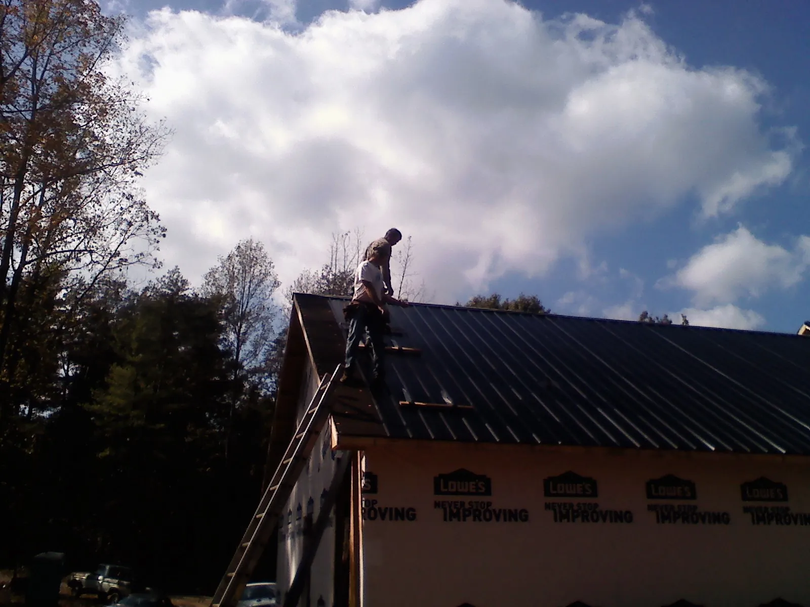 Roofer fastening dark metal panels high against a cloudy sky, from a Roof Inspection job in Ward
