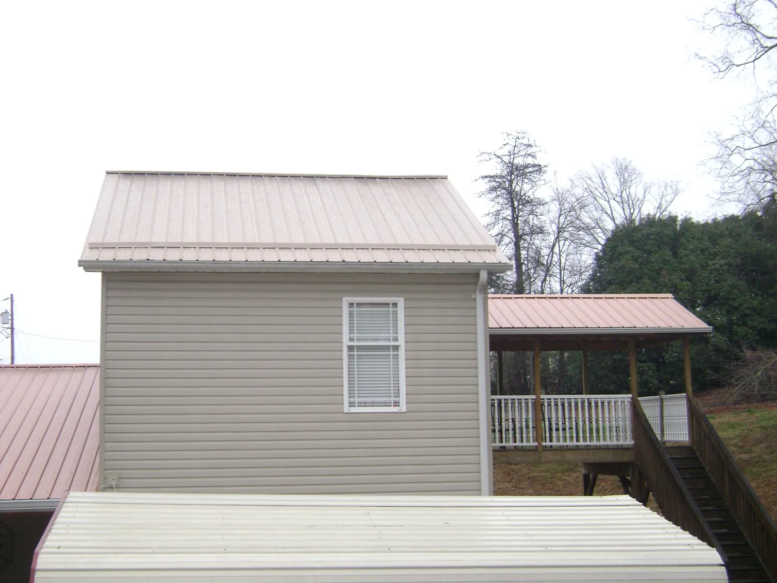 Tan metal roofs on a two story addition and attached porch, from a Roof Replacement job in Ward